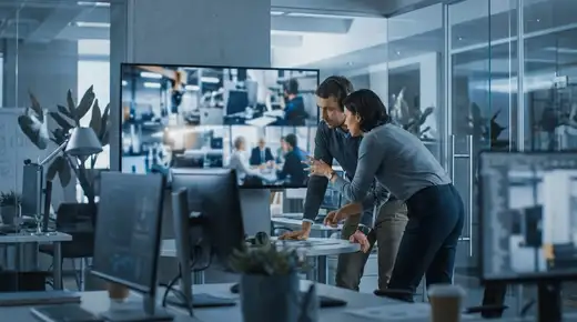 Deux professionnels en open space passant en revue des plans vidéo sur un grand écran, ambiance cinématique aux tons bleus